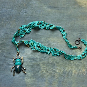 May include: A turquoise and brown beaded necklace with a beetle pendant. The necklace is made of small beads and has a delicate, intricate design. The beetle pendant is made of metal and has a turquoise and black enamel finish.