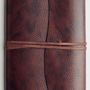 May include: A brown leather-bound journal with a textured surface and a leather strap closure.
