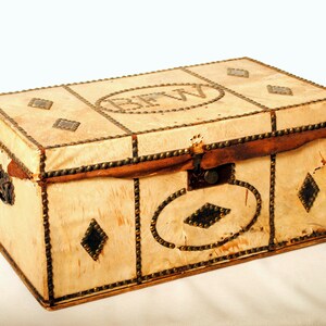 May include: A vintage leather-covered trunk with brass studs and a leather strap. The trunk has a brass lock and two brass handles. The trunk is decorated with a diamond pattern and the initials "BFW" are embossed on the top.