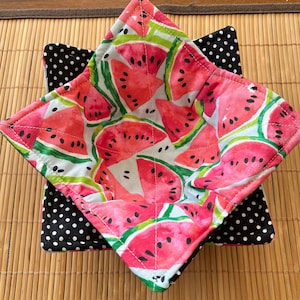 May include: A set of two quilted pot holders featuring a watermelon print. The larger pot holder has a white background with red and green watermelon slices. The smaller pot holder has a black background with white polka dots.