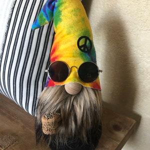 May include: A tie-dye gnome with a peace sign on its hat, wearing round sunglasses and holding a cork.