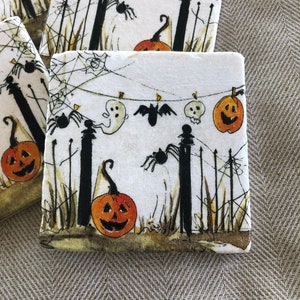 May include: Square Halloween-themed coasters with a white background. The coasters feature a spooky design with orange jack-o'-lanterns, black spiders, ghosts, and bats. Black fence posts and spiderwebs complete the festive look.