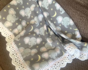 May include: A gray fleece blanket featuring a repeating pattern of elephants, stars, and crescent moons. The blanket is trimmed with a white crocheted lace border with a pink accent. This blanket is ideal for a baby.