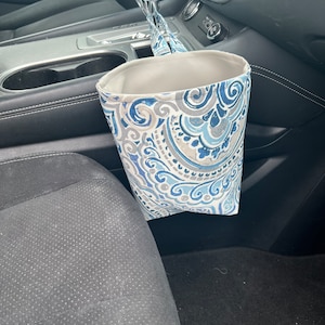 May include: A gray and blue patterned fabric trash can hanging from the side of a car seat.