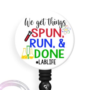 May include: White badge reel with a black retractable cord and a round button with the text "We get things SPUN, RUN, & DONE #LABLIFE". The button has a red test tube, a blue beaker, a green beaker, and a yellow atom symbol.