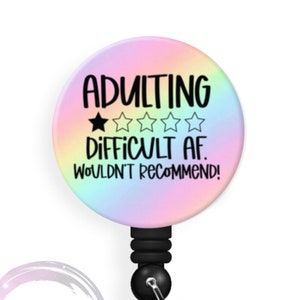 May include: A rainbow-colored badge reel with a black retractable cord and a white clip. The badge holder features a white background with black text that reads "Adulting 1 star out of 5 stars Difficult AF. Wouldn't recommend!"