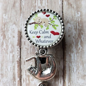 May include: A silver retractable badge holder with a round charm featuring a cartoon sloth sleeping on a branch with red hearts and the text "Keep Calm and Whatever".
