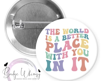 May include: A white button with a colorful text design that reads "The world is a better place with you in it". The text is in a rainbow color scheme with a pink, yellow, green, blue, and purple color scheme.