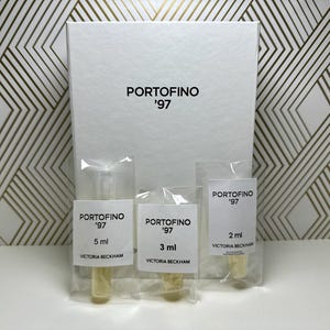 May include: Three clear glass perfume sample bottles with white labels. The labels read "PORTOFINO '97" and list the volume in milliliters: 5 ml, 3 ml, and 2 ml. The labels also include the brand name "VICTORIA BECKHAM".