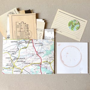 Op de afbeelding: Een verzameling papieren ephemera, waaronder een envelop met kaartpatroon gevuld met kaarten in vintage-stijl, een gelinieerde kaart met een ronde kaartuitsnede en een vierkante witte kaart met een vage, ronde bruine koffievlek.
