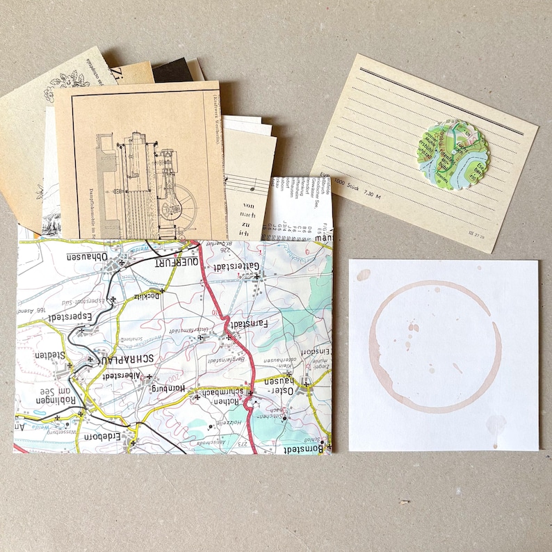 Op de afbeelding: Een verzameling papieren ephemera, waaronder een envelop met kaartpatroon gevuld met kaarten in vintage-stijl, een gelinieerde kaart met een ronde kaartuitsnede en een vierkante witte kaart met een vage, ronde bruine koffievlek.