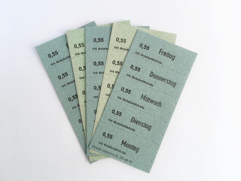 Op de afbeelding: Een waaiervormige opstelling van vijf rechthoekige papieren kaartjes in tinten saliegroen en licht olijfgroen. Elk kaartje bevat zwarte gedrukte tekst, waaronder het getal 0,55, OS Reinholdshain en de dagen van de week: Montag, Dienstag, Mittwoch, Donnerstag en Freitag.