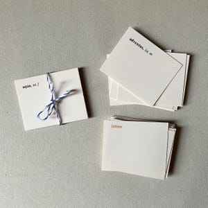 Op de afbeelding: Een verzameling rechthoekige witte kaarten met gedrukte tekst. E&eacute;n stapel is samengebonden met blauw en wit touw en toont de tekst 'aqua, ae f'. Een andere stapel toont 'adventus, ūs m' in het zwart en een derde stapel 'lieben' in oranje.