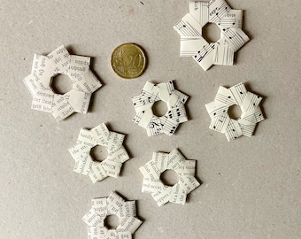 May include: Seven white paper stars with a hole in the center. The stars are made from pages of a book with black text. The text is visible on the stars.