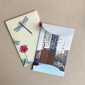 May include: Two envelopes, one with a white background and a dragonfly and flower design, the other with a photo of a modern building with a blue and white facade.