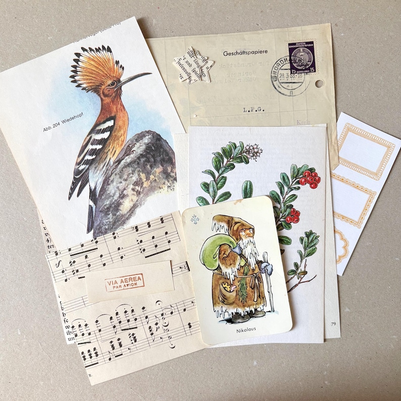 Op de afbeelding: Een verzameling vintage papieren ephemera, waaronder een prent van een hop met het label Abb. 204 Wiedehopf, een bladmuziek met een Via Aerea Par Avion-stempel, een kaart met een bebaarde figuur genaamd Nikolaus en een botanische illustratie.