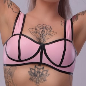 May include: A pink latex bra with black trim. The bra has a geometric design and is made of a smooth, shiny material.