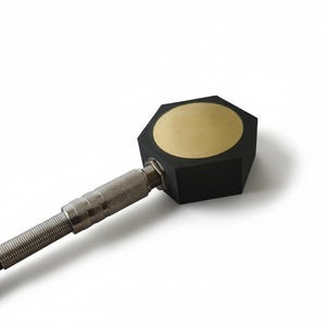 May include: A black and gold hexagonal device with a silver connector and a black cable. The device has a gold circular surface on top. The silver connector is ribbed. The background is white.