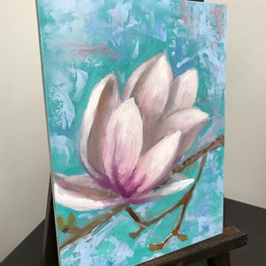 May include: A close-up of a painting of a pink magnolia flower with a light blue background. The flower is painted in a realistic style with visible brushstrokes.