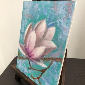May include: A painting of a single pink magnolia flower on a branch against a turquoise blue background. The flower is painted in a realistic style with visible brushstrokes.