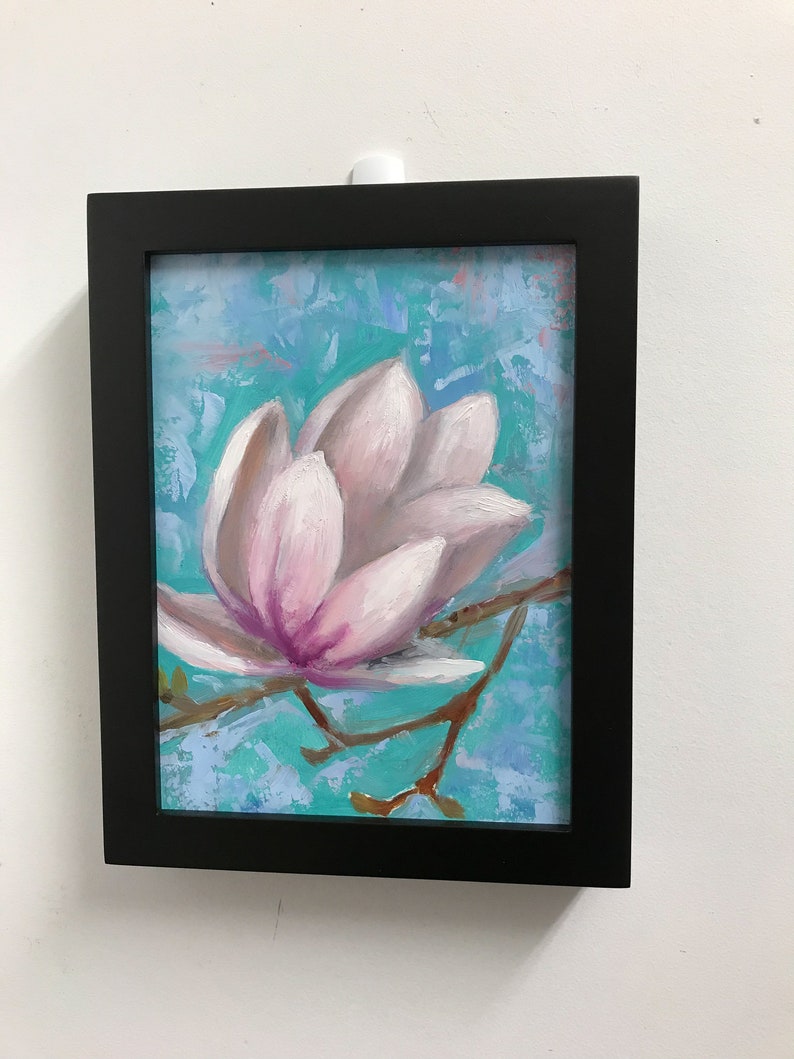 May include: A framed painting of a pink magnolia flower with a light blue and white background.