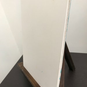 May include: A white canvas on a wooden easel. The canvas is blank and ready for painting.