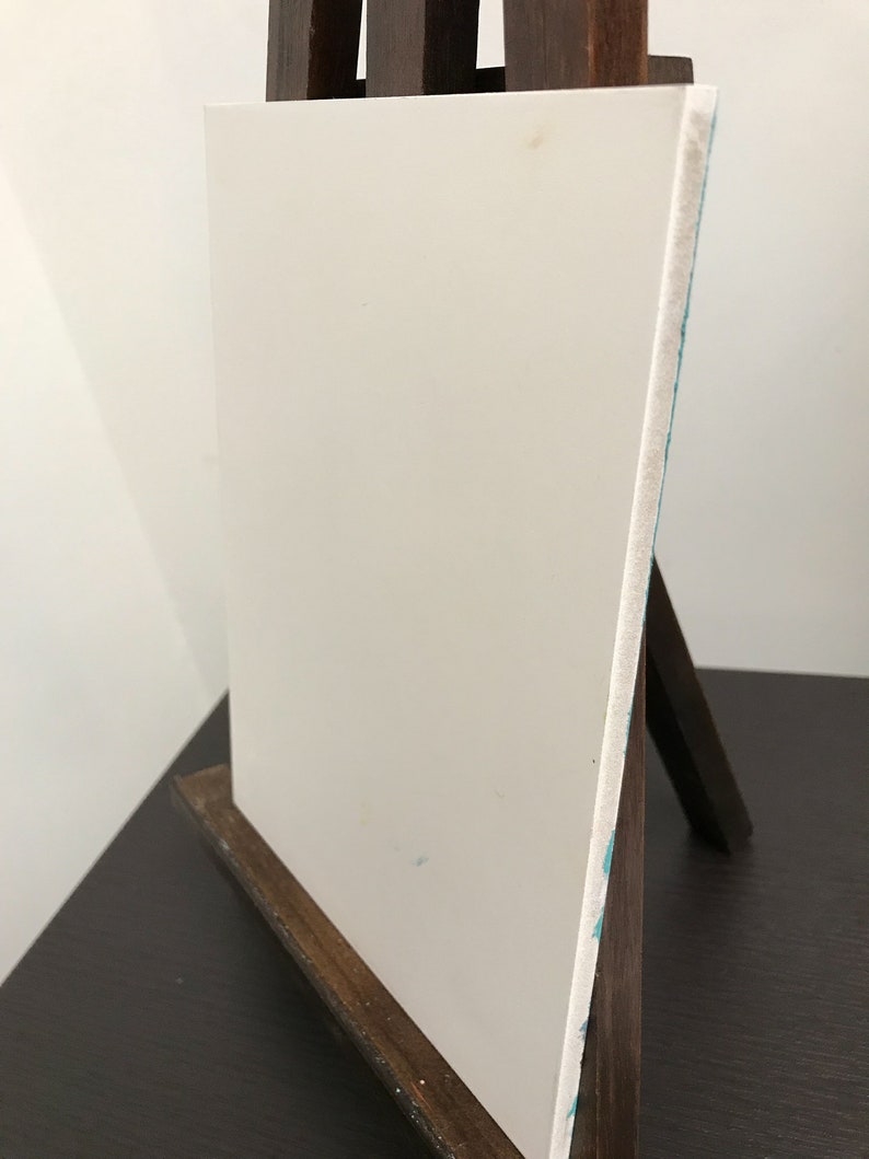 May include: A white canvas on a wooden easel. The canvas is blank and ready for painting.