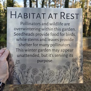 May include: A rectangular metal garden sign with the words "HABITAT AT REST" in black. The sign has a floral border and text describing the garden's purpose for pollinators and wildlife during winter.