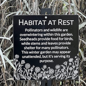 May include: A black rectangular sign with white text that reads "HABITAT AT REST." The sign explains the garden's purpose for pollinators and wildlife during winter. Floral illustrations decorate the bottom edge of the sign.