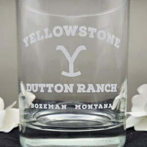 May include: A clear glass tumbler with the words "YELLOWSTONE" arched across the top and "DUTTON RANCH" below. The text "BOZEMAN MONTANA" is at the bottom. The glass has a simple, elegant design.