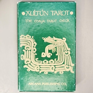 May include: A rectangular green box for the Xultún Tarot: The Maya Tarot Deck. The front features cream-colored line art of a stylized serpent or dragon figure. The text reads Xultún Tarot, The Maya Tarot Deck, and Arcana Publishing Co.