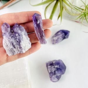 May include: Four amethyst crystal points in various sizes and shapes. The crystals are a deep purple color with some white inclusions.