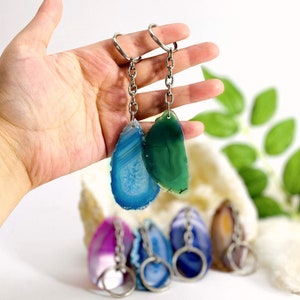 Op de afbeelding: Een set van vijf agaat-schijf sleutelhangers. De sleutelhangers zijn gemaakt van natuurlijke agaat-schijven in verschillende kleuren, waaronder blauw, groen, paars en bruin. Elke schijf is bevestigd aan een zilveren sleutelring.