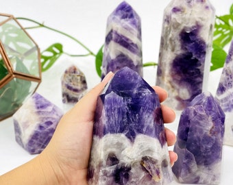 May include: A collection of amethyst crystal points in various sizes and shades of purple. The crystals have a natural, raw look and are arranged on a white surface.