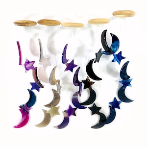May include: A crystal mobile with multiple agate crescent moons and stars hanging from wooden dowels. The moons are in shades of purple, blue, black, and brown. The stars are in shades of purple and blue.