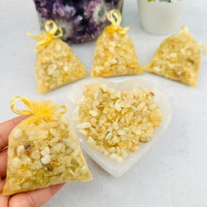 May include: Five small yellow crystal bags filled with yellow citrine chips. The bags are made of yellow tulle and have a yellow ribbon tie. The crystals are displayed on a white heart-shaped dish.