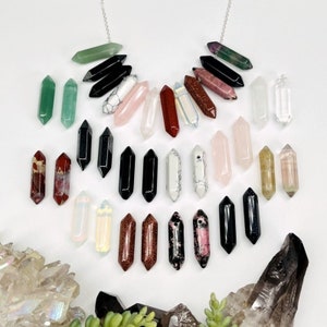 May include: A collection of 20 different colored crystal points, including clear, pink, green, red, black, and brown. The points are arranged in a semi-circle shape, with a silver chain running through the top of each point.
