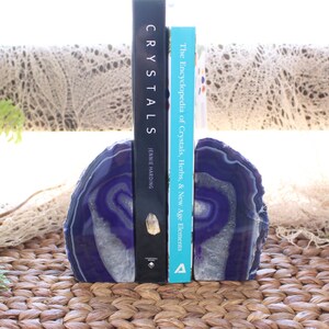 May include: Purple agate bookends with a white and purple swirl pattern. The bookends are holding up two books, one titled "Crystals" and the other titled "The Encyclopedia of Crystals, Herbs, & New Age Elements".