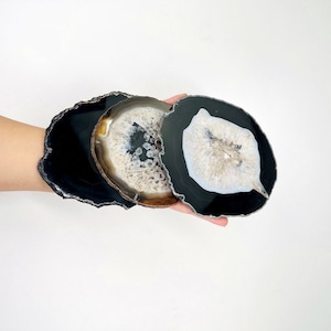 May include: Three agate coasters with natural edges. The coasters feature a black outer ring with a white and gray center. The coasters are round and vary in size. These coasters are ideal for home decor.