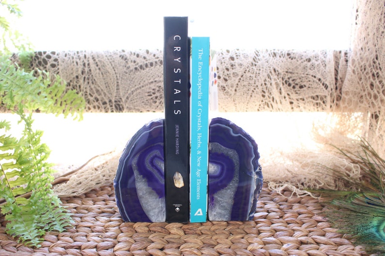 May include: Purple agate bookends with a white and purple swirl pattern. The bookends are holding up two books, one titled "Crystals" and the other titled "The Encyclopedia of Crystals, Herbs, & New Age Elements".