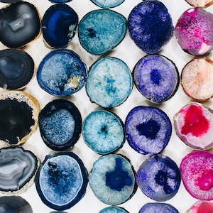 May include: Assortment of agate slices in various colors and patterns, including blue, pink, purple, and gray. The slices are polished and have a smooth, shiny surface.