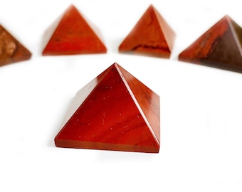 May include: Five red carnelian crystal pyramids on a white background. The pyramids are all the same size and shape, and they are arranged in a semi-circle.