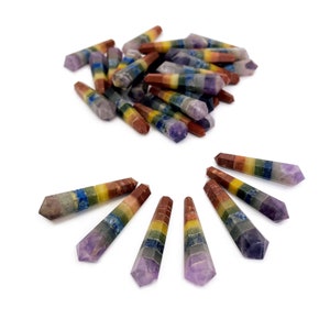 May include: A collection of colorful, hexagonal-shaped crystal wands. Each wand features a gradient of colors, including purple, blue, green, yellow, orange, and brown. Some wands are arranged in a fan shape, while others are in a pile.
