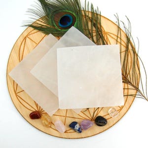May include: Three white selenite charging plates on a wooden base with a peacock feather and various crystals.