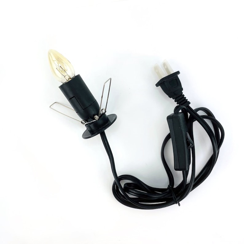 K&ouml;nnte beinhalten: Schwarze elektrische Kerze mit einer klaren Gl&uuml;hbirne und einem schwarzen Kabel mit einem Ein-/Ausschalter und einem Stecker.