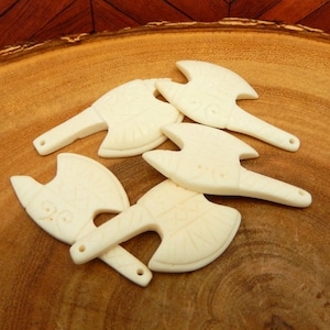 May include: Five white bone axe pendants with intricate carvings. The pendants are arranged on a wooden surface.