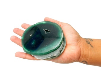 May include: A set of four green agate coasters with a natural, irregular shape. The coasters are stacked on top of each other, with the top coaster having a small hole in the center.