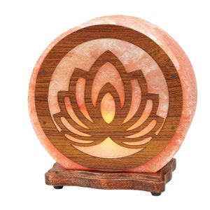 K&ouml;nnte beinhalten: Eine runde Himalaya-Salzlampe mit einem Holzsockel und einem geschnitzten Lotusbl&uuml;ten-Design. Die Lampe ist eingeschaltet und leuchtet.