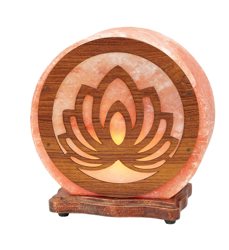 K&ouml;nnte beinhalten: Eine runde Himalaya-Salzlampe mit einem Holzsockel und einem geschnitzten Lotusbl&uuml;ten-Design. Die Lampe ist eingeschaltet und leuchtet.
