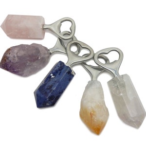 May include: Five crystal bottle openers with silver metal handles. The crystals are amethyst, rose quartz, clear quartz, blue quartz, and citrine.